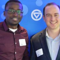 Two alumni pose for a photo together behind the Laker background